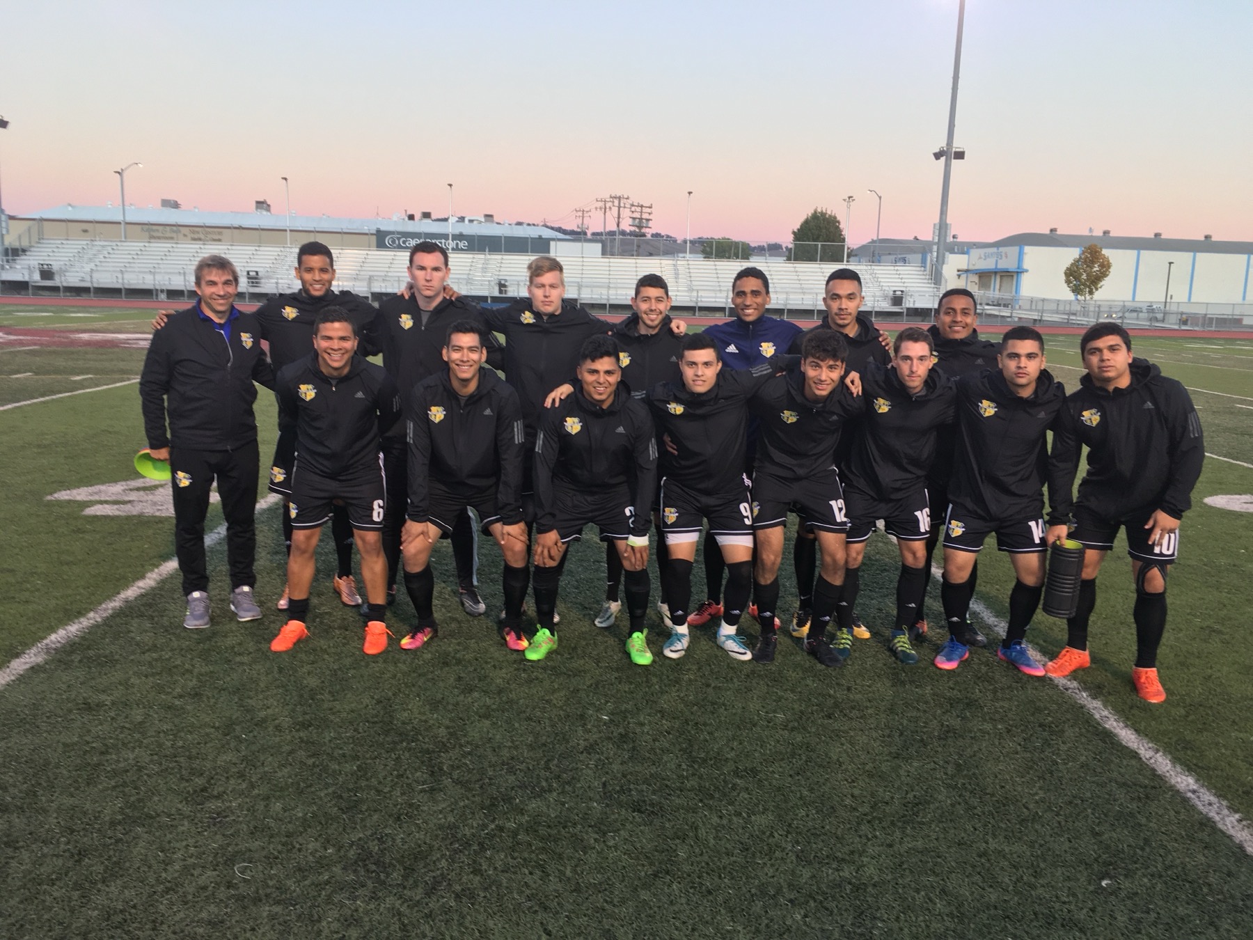 Cal Victory FC team in black kits posing on the field at sunset
