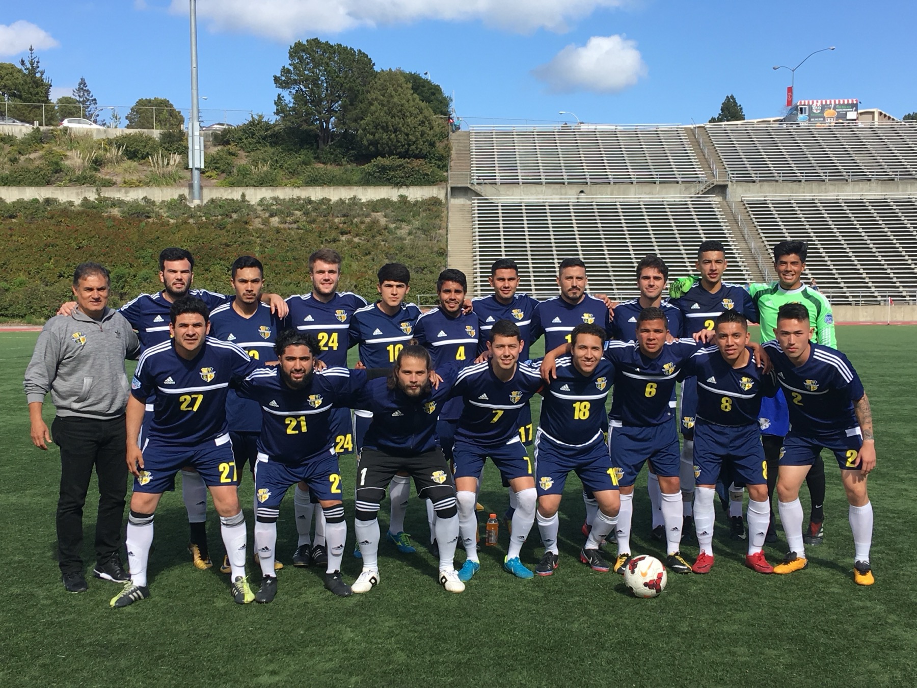 Cal Victory FC team in navy kits posing on the field during the day